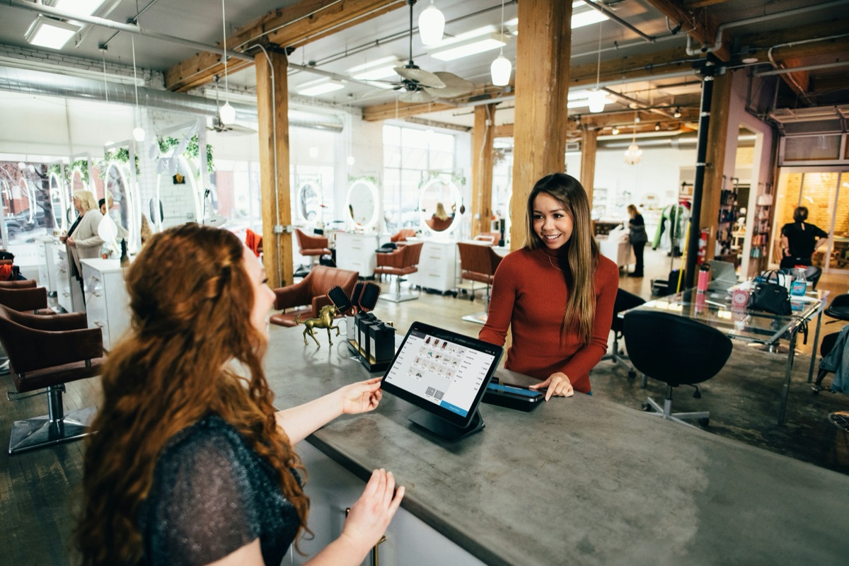 Salon receptionist checking in a smiling customer at the front desk